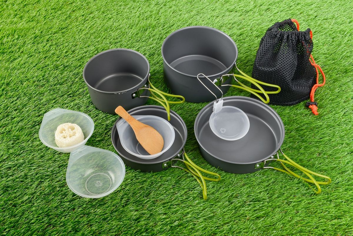 Cooking set pots for backpacker or journey use for outdoor camping placed on green grass background, copy space for design elements.