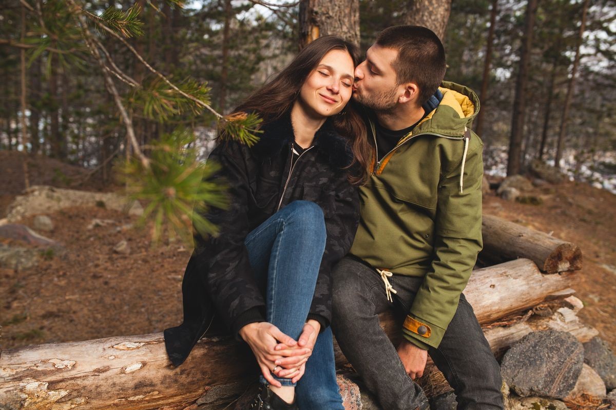 young beautiful hipster man and woman in love traveling together in wild nature, hiking in forest, autumn style apparel, coat, romance, vacation, kiss, smiling, happy